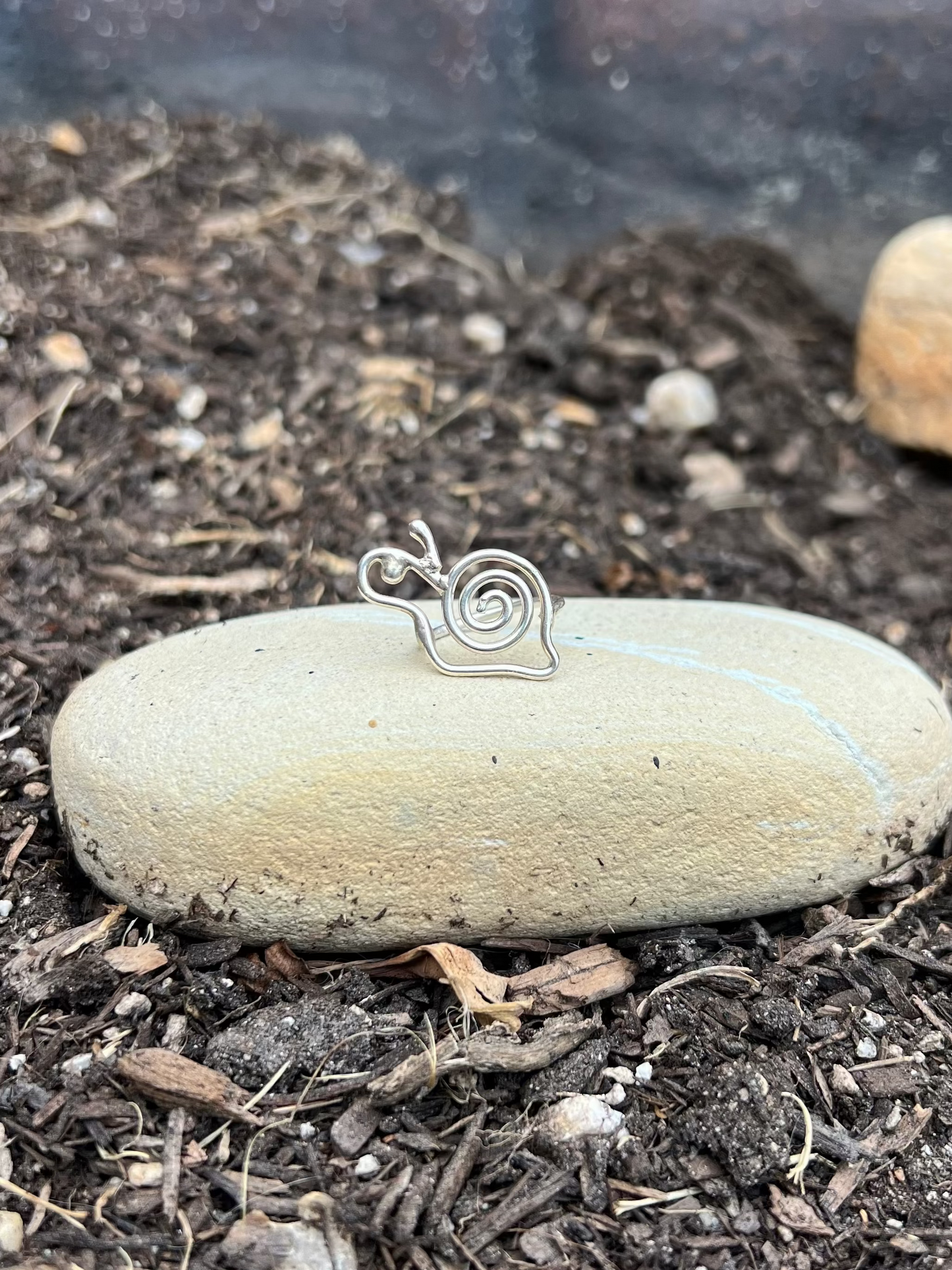 Silver snail-shaped pendant on a stone in a garden setting