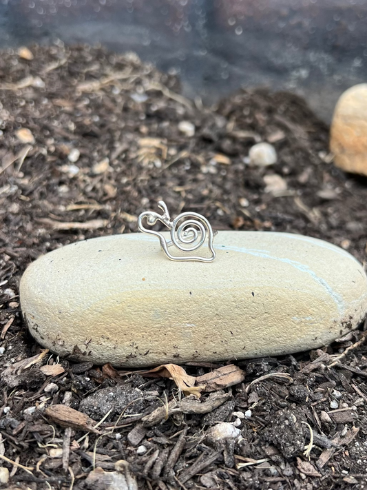 Silver snail-shaped pendant on a stone in a garden setting