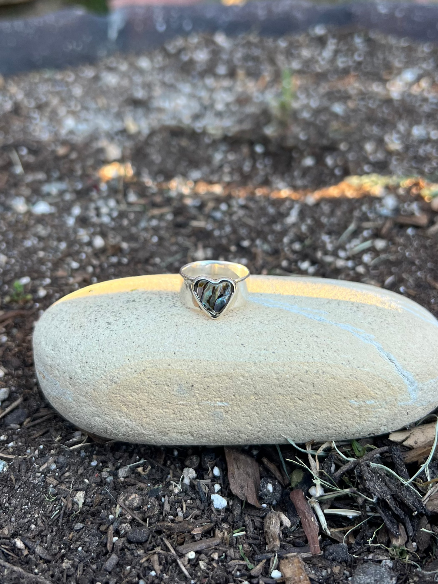 shell heart ring sitting on a stone in a garden