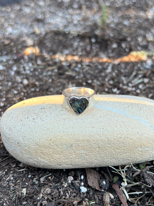 Small stone with a heart-shaped hole on a bed of soil and small rocks.