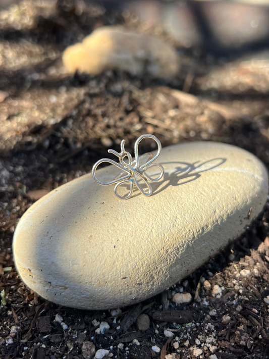 Small silver wire sculpture on a smooth stone in a garden setting