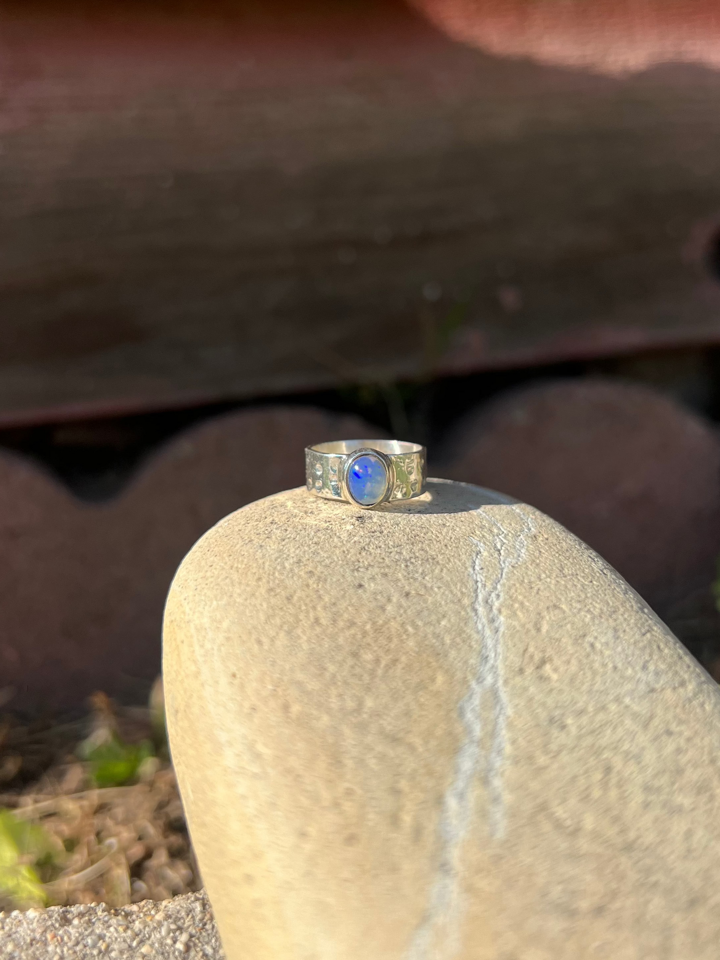 Silver ring with a blue stone on a rock with a wooden background