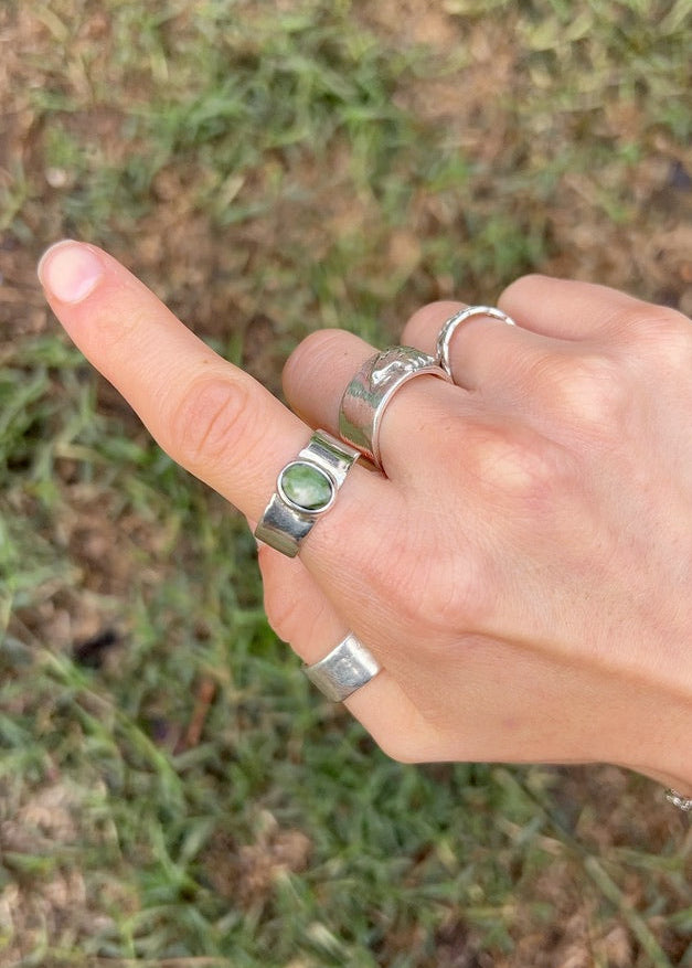 Hand with multiple silver rings on a grassy background
