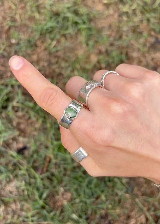 Hand with multiple silver rings on a grassy background