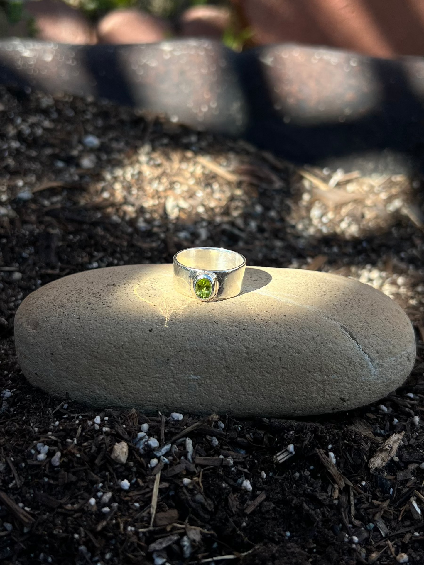 Small silver ring with a green gemstone on a rock in a garden setting