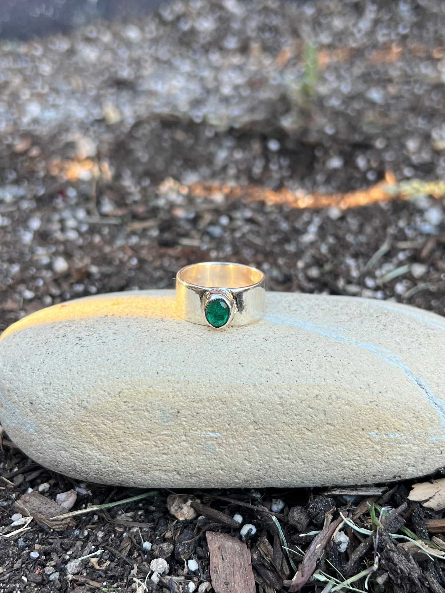 silver ring with a green gemstone on a stone in a garden setting