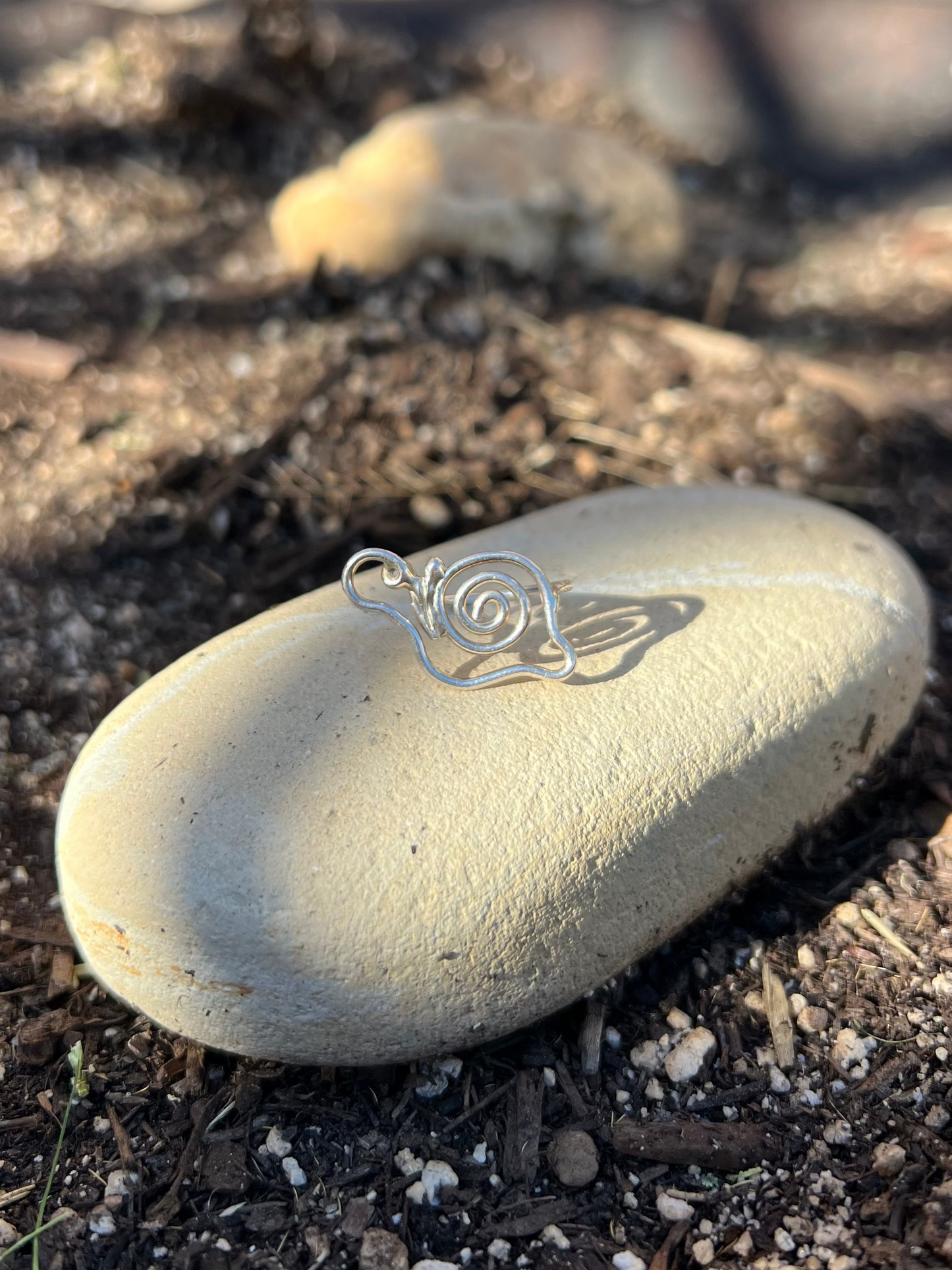 Silver wire-wrapped pendant on a smooth stone in a garden setting