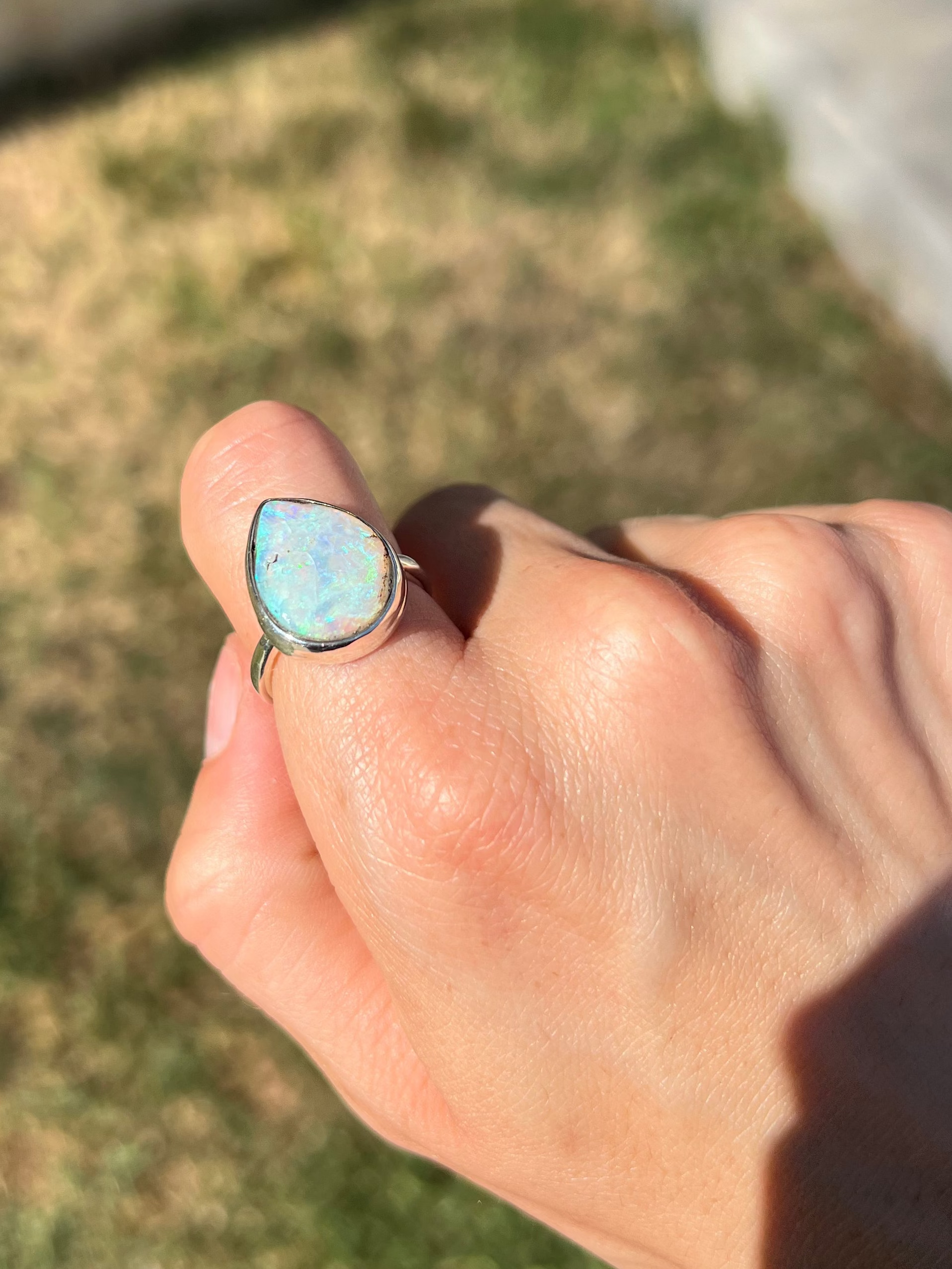 Hand wearing a ring with an opal stone outdoors