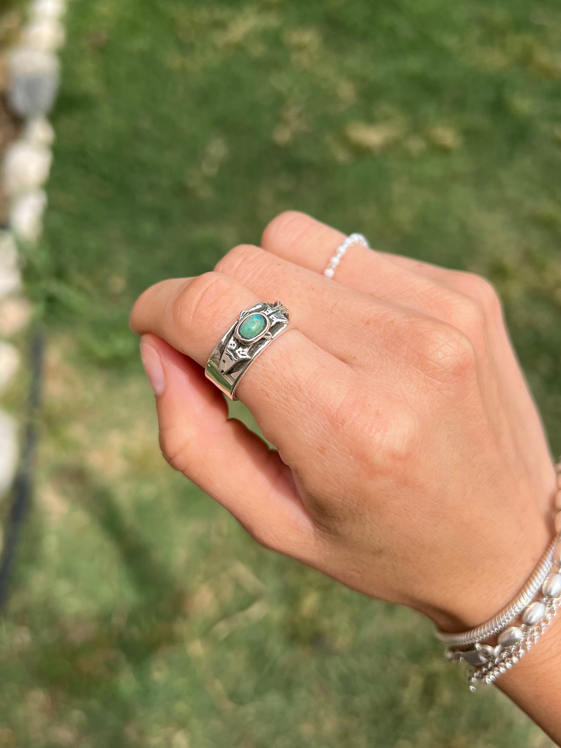 Hand wearing a silver ring with a turquoise stone against a blurred green background