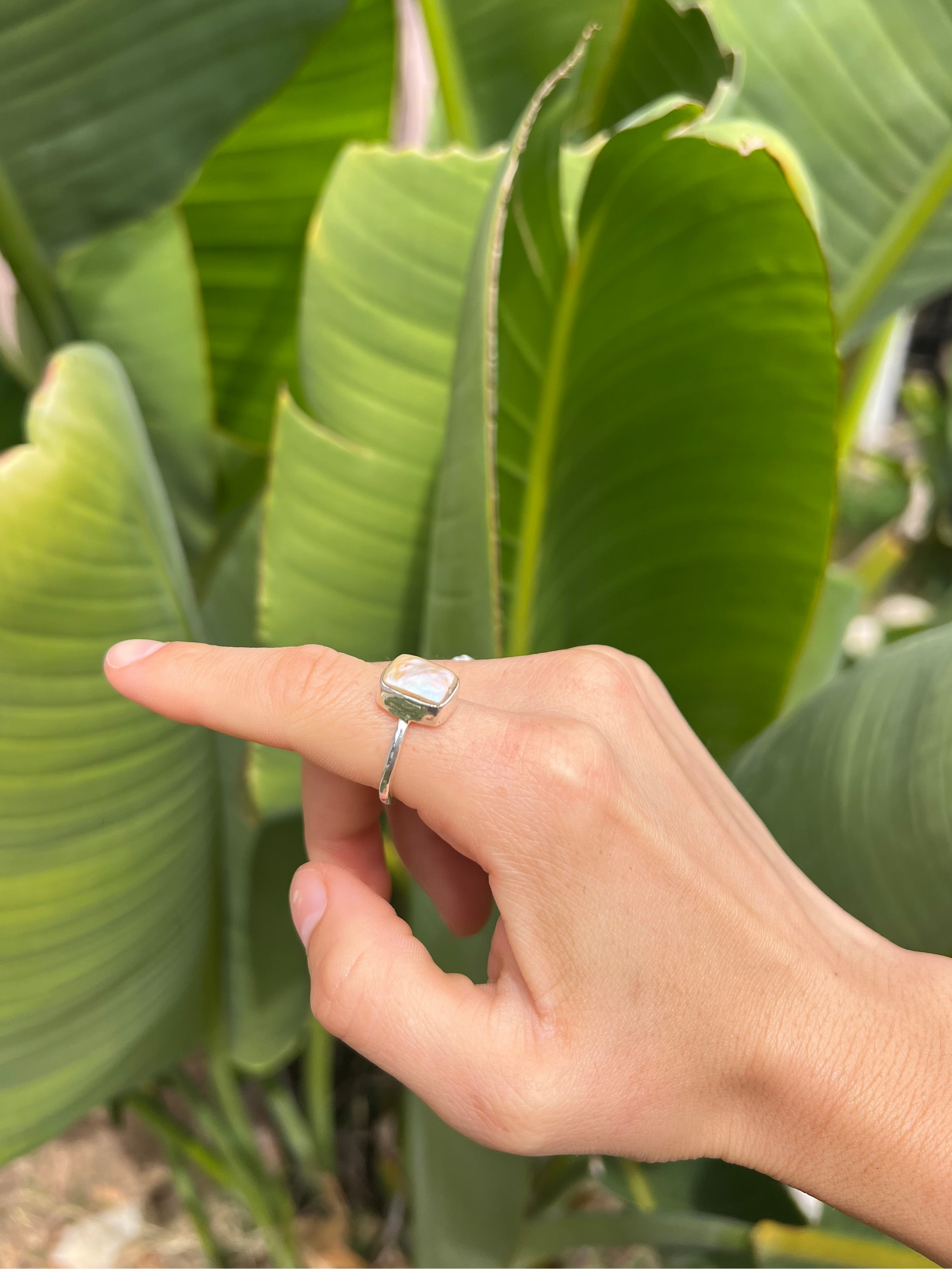 Hand wearing a ring with a green leafy background