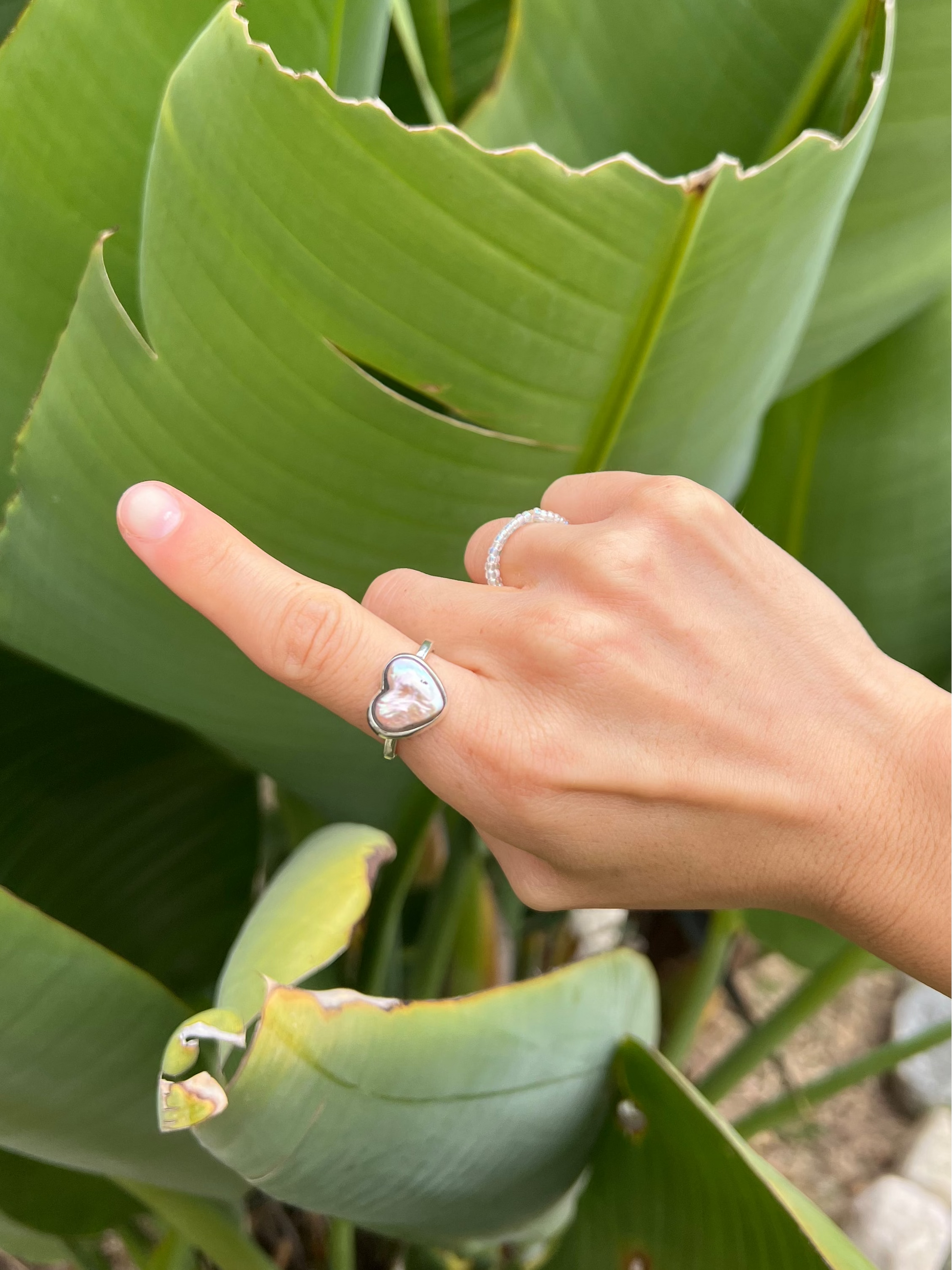 Hand with a heart-shaped ring pointing to a large green leaf