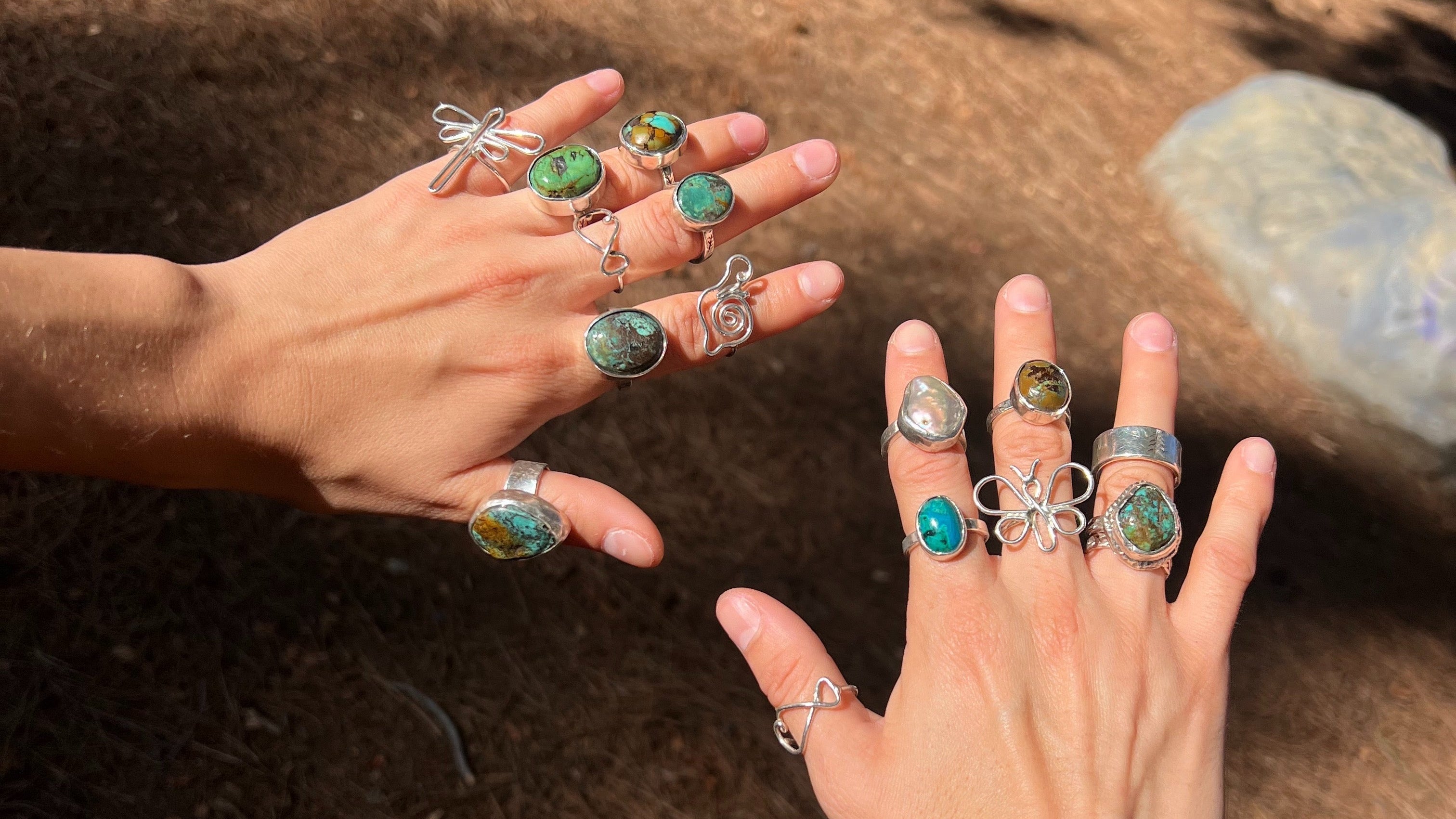 Two hands wearing multiple rings with green and silver jewelry against a natural background.