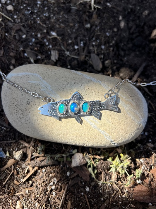 Silver necklace with a fish-shaped pendant featuring three colored stones on a rock.