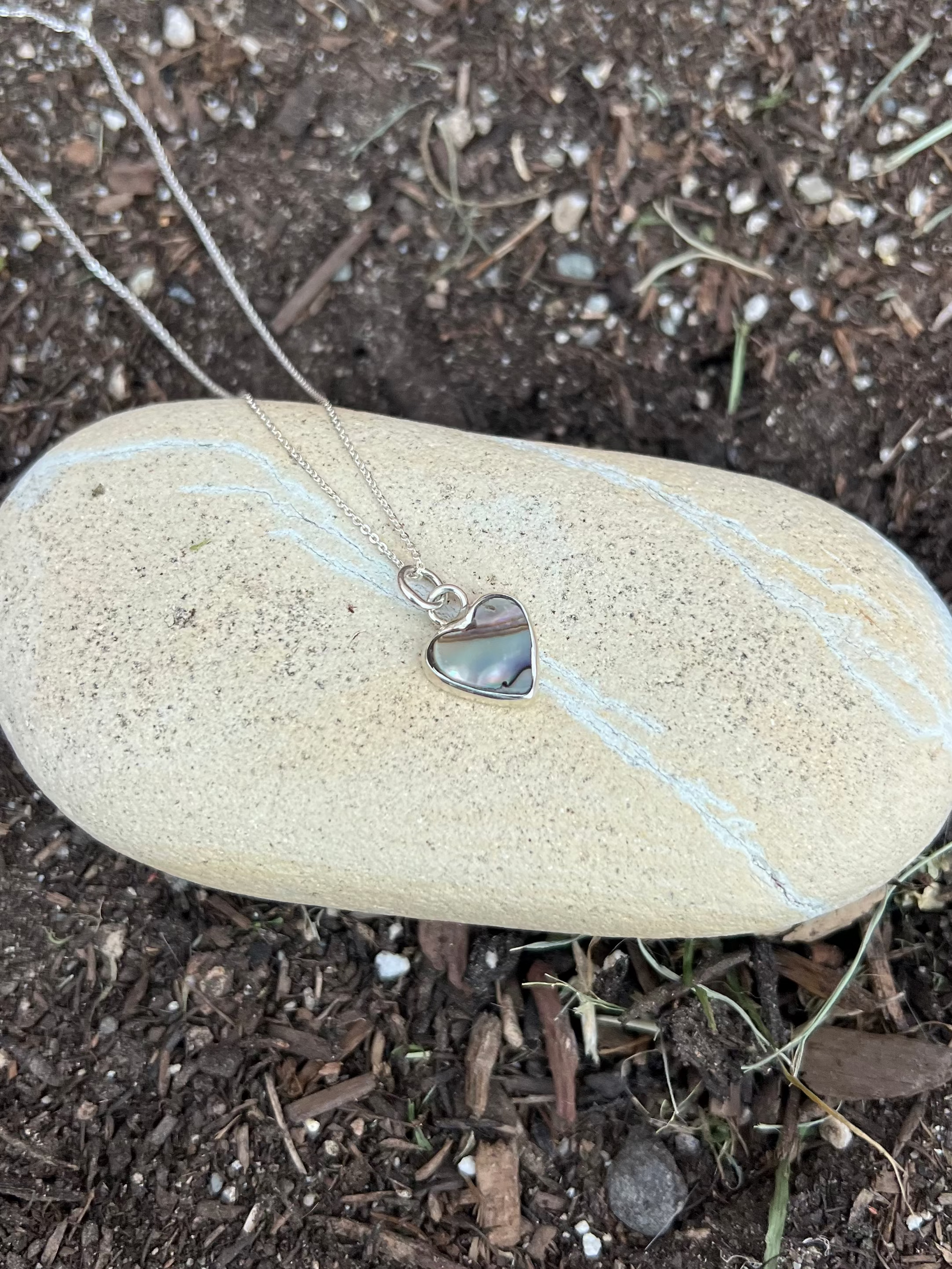 abalone shell heart silver necklace  on a rock