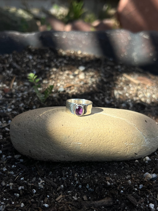 Silver ring with a purple gemstone on a stone in a garden setting