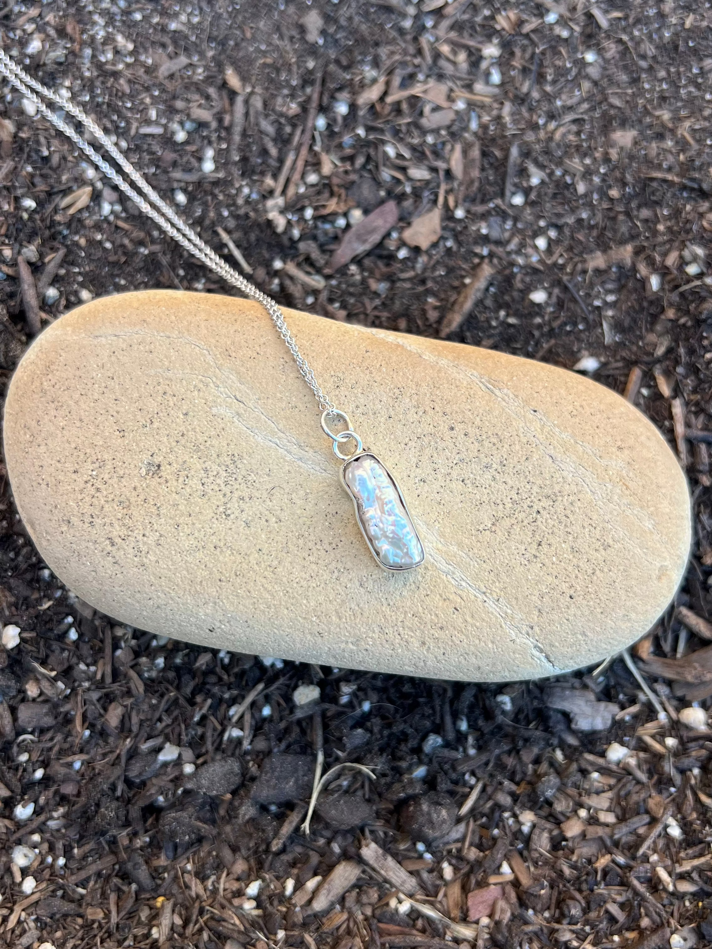 Silver necklace with a pendant on a rock outdoors