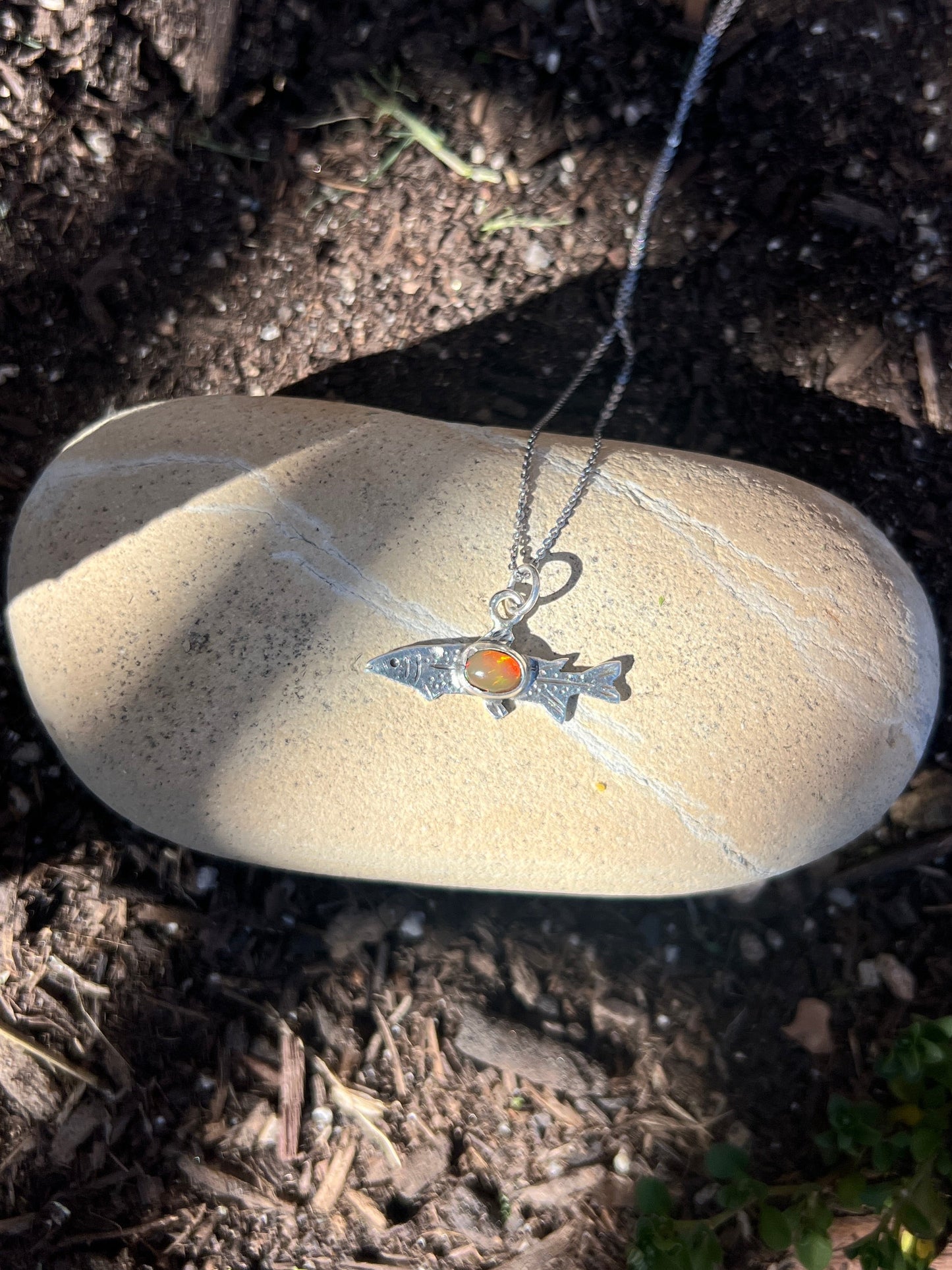 Silver necklace with a pendant on a rock in a natural setting