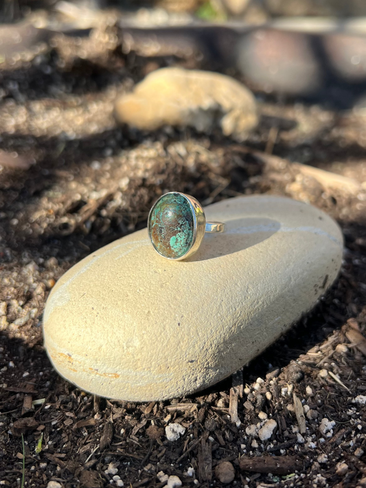 Ring with a green gemstone on a rock outdoors
