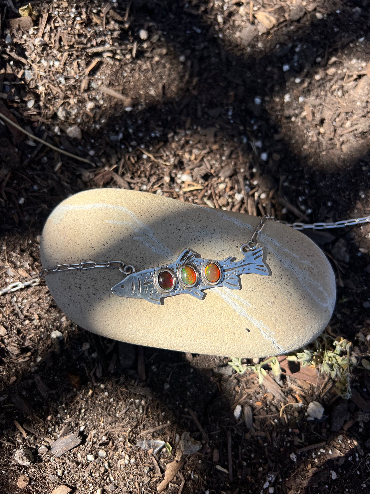 Necklace with a silver pendant featuring three stones on a rock outdoors