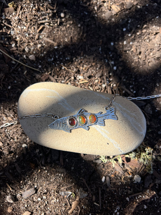 Necklace with a silver pendant featuring three stones on a rock outdoors
