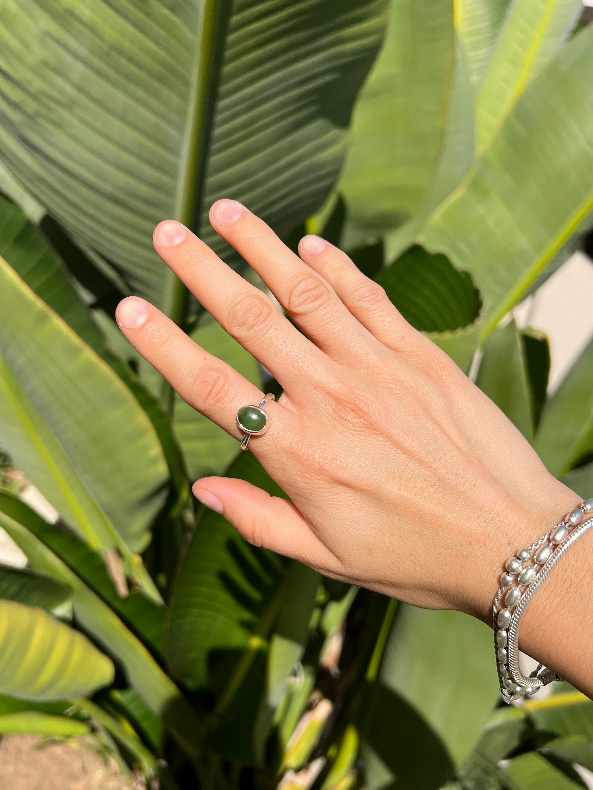 Hand with a ring and bracelet in front of green leaves