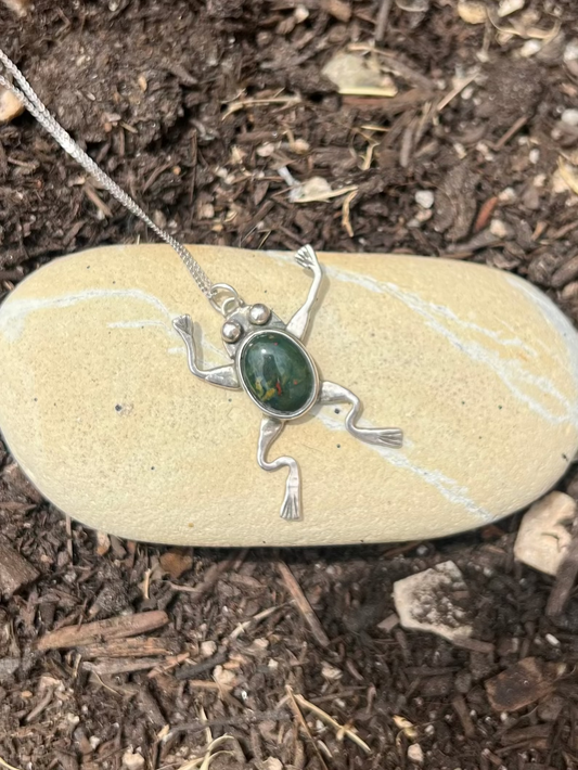 Frog pendant necklace on a stone with soil background