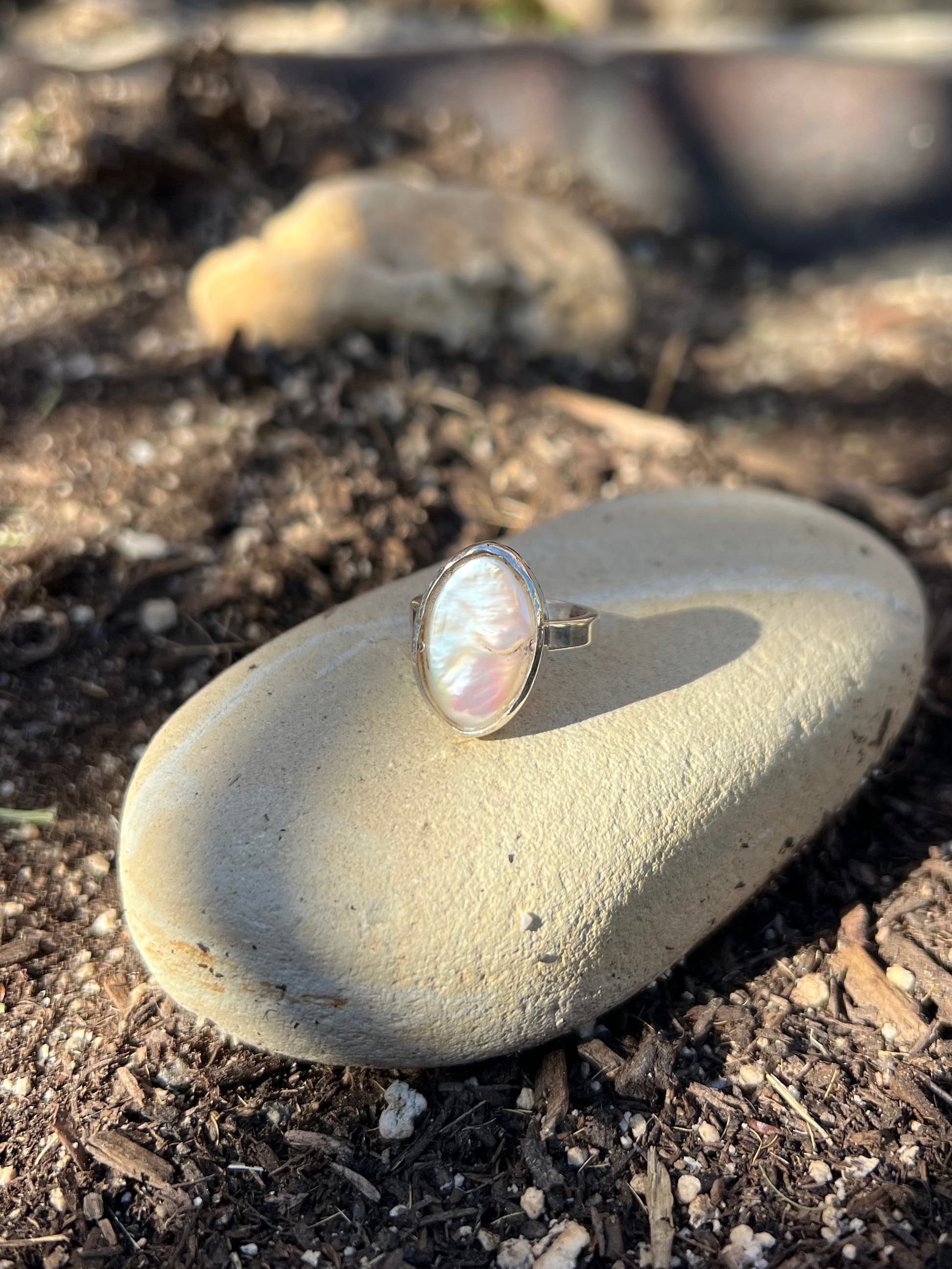 Ring with a pearl-like stone on a rock in an outdoor setting