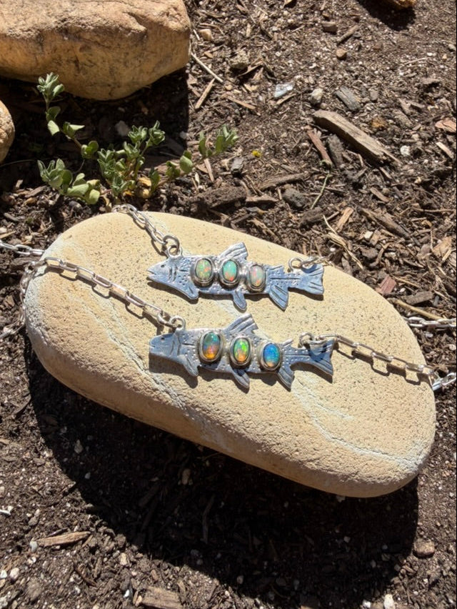 Pair of silver fish-shaped earrings with embedded stones on a rock outdoors.
