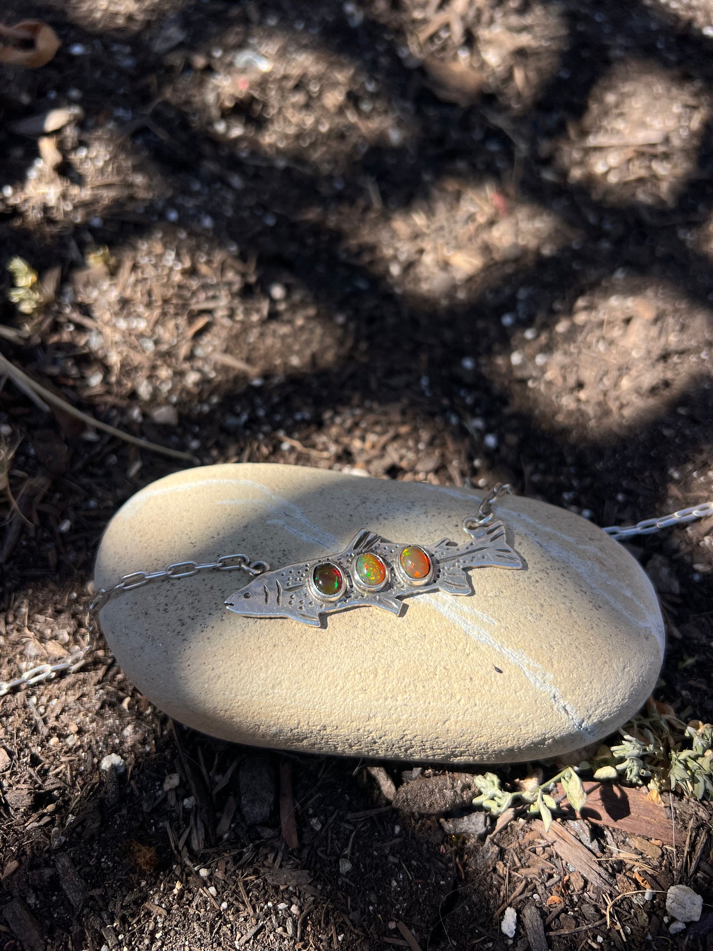 Silver necklace with colorful stones on a stone in a natural setting