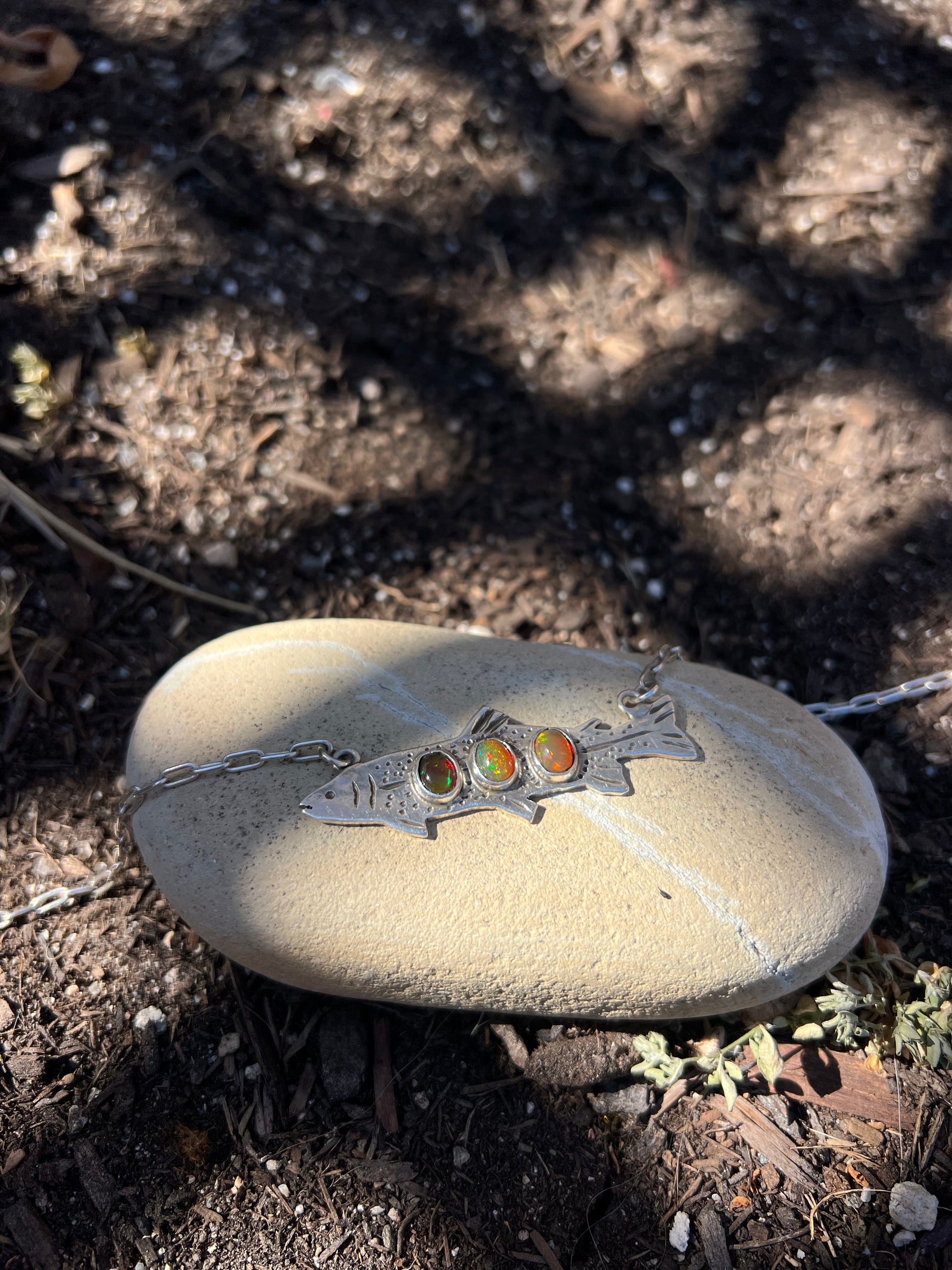 Silver necklace with colorful stones on a stone in a natural setting