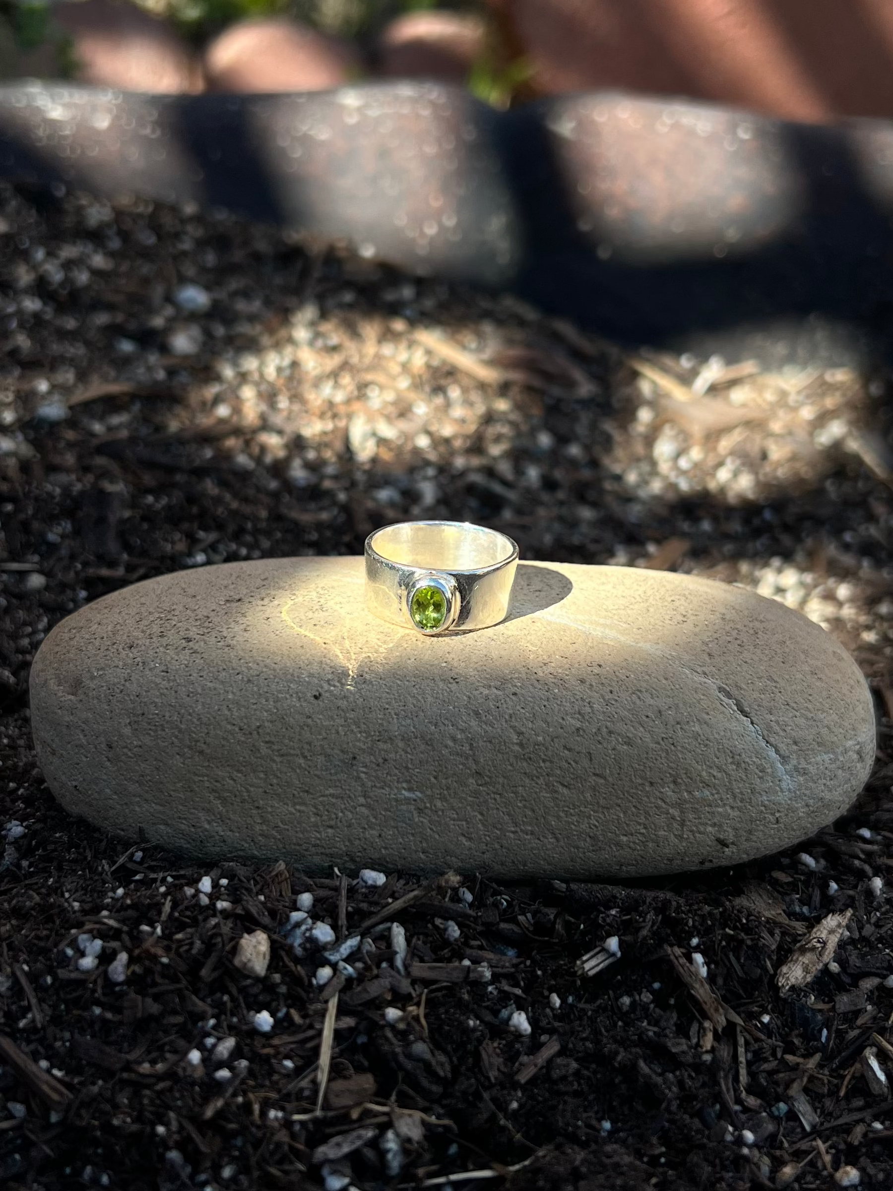 Small silver ring with a green gemstone on a rock in a garden setting