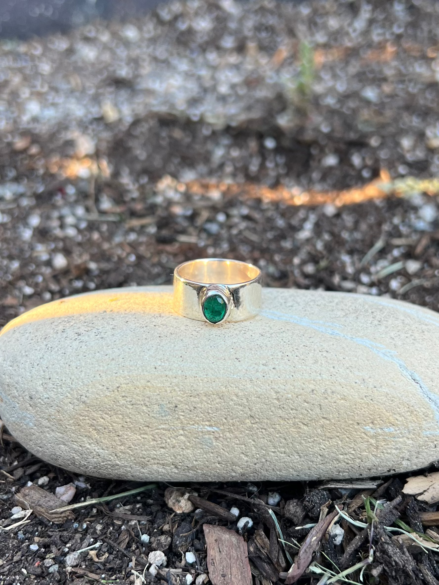 silver ring with a green gemstone on a stone in a garden setting