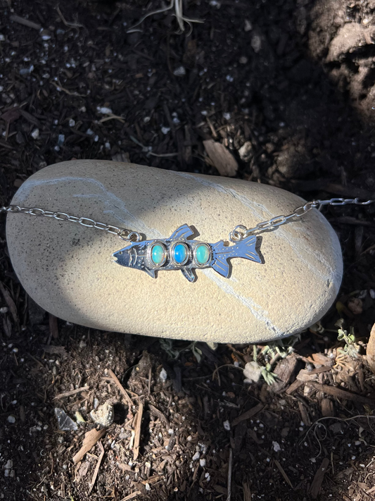 Necklace with a fish pendant on a pebble outdoors