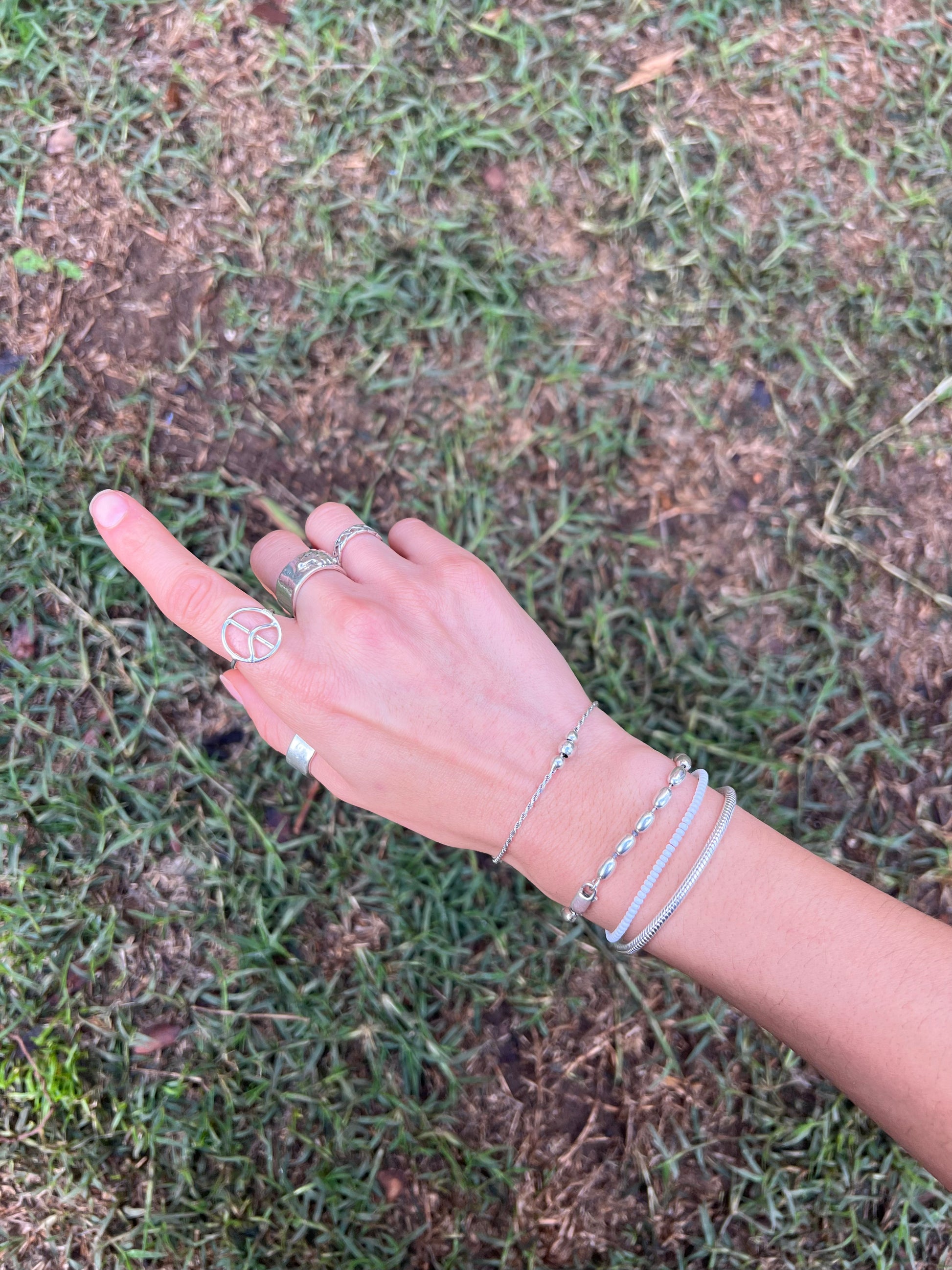 Hand with multiple silver rings and bracelets on a grassy background
