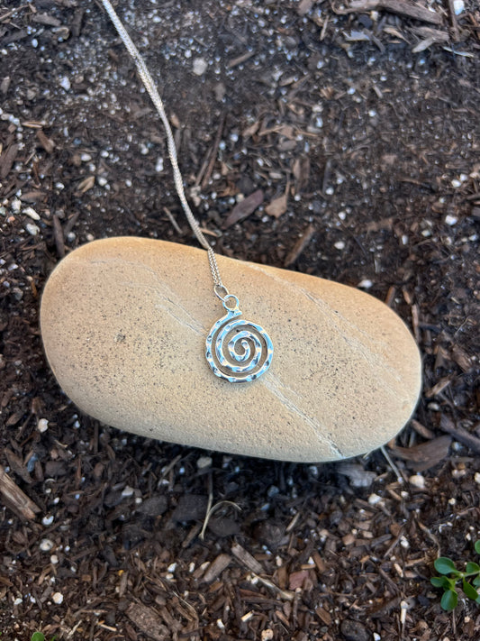 Silver spiral pendant necklace on a rock outdoors