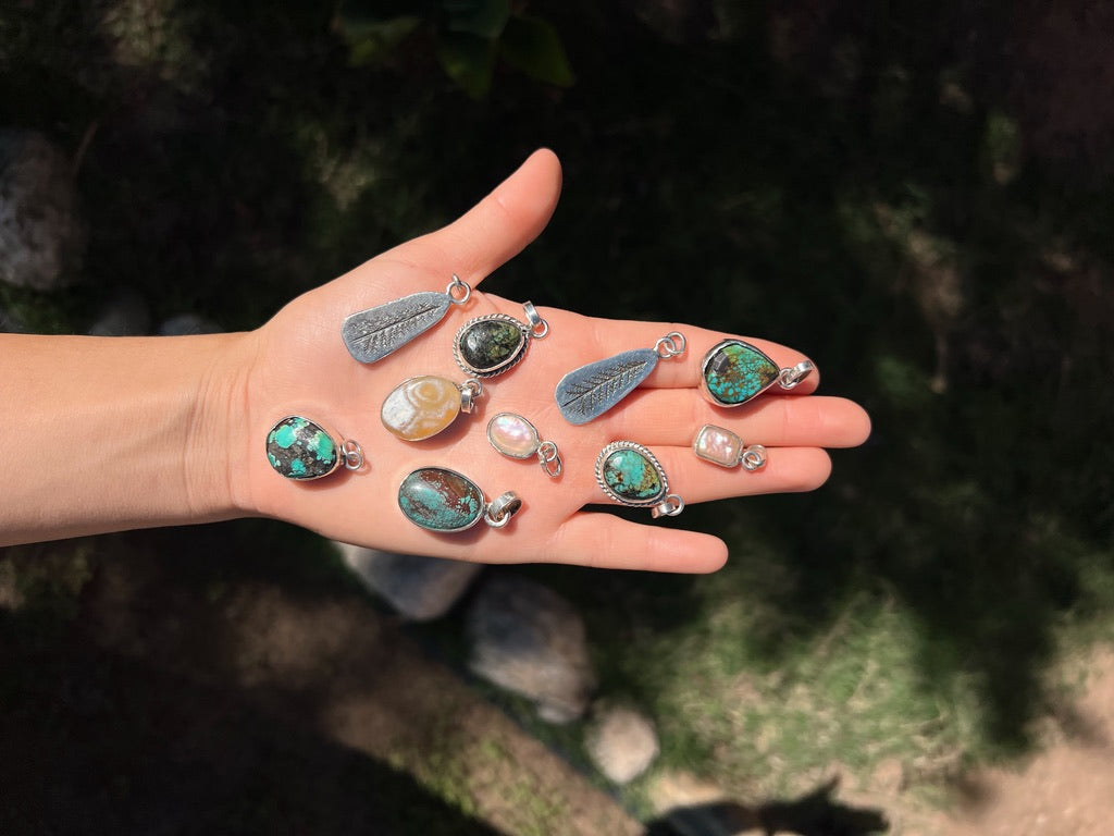 Hand holding multiple pendants with various designs and colors against a natural background