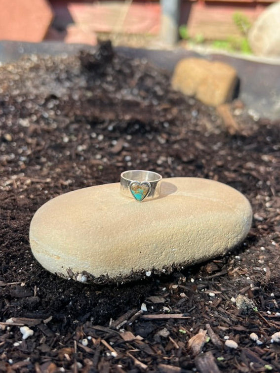 Silver ring with a green stone on a rock in a garden setting
