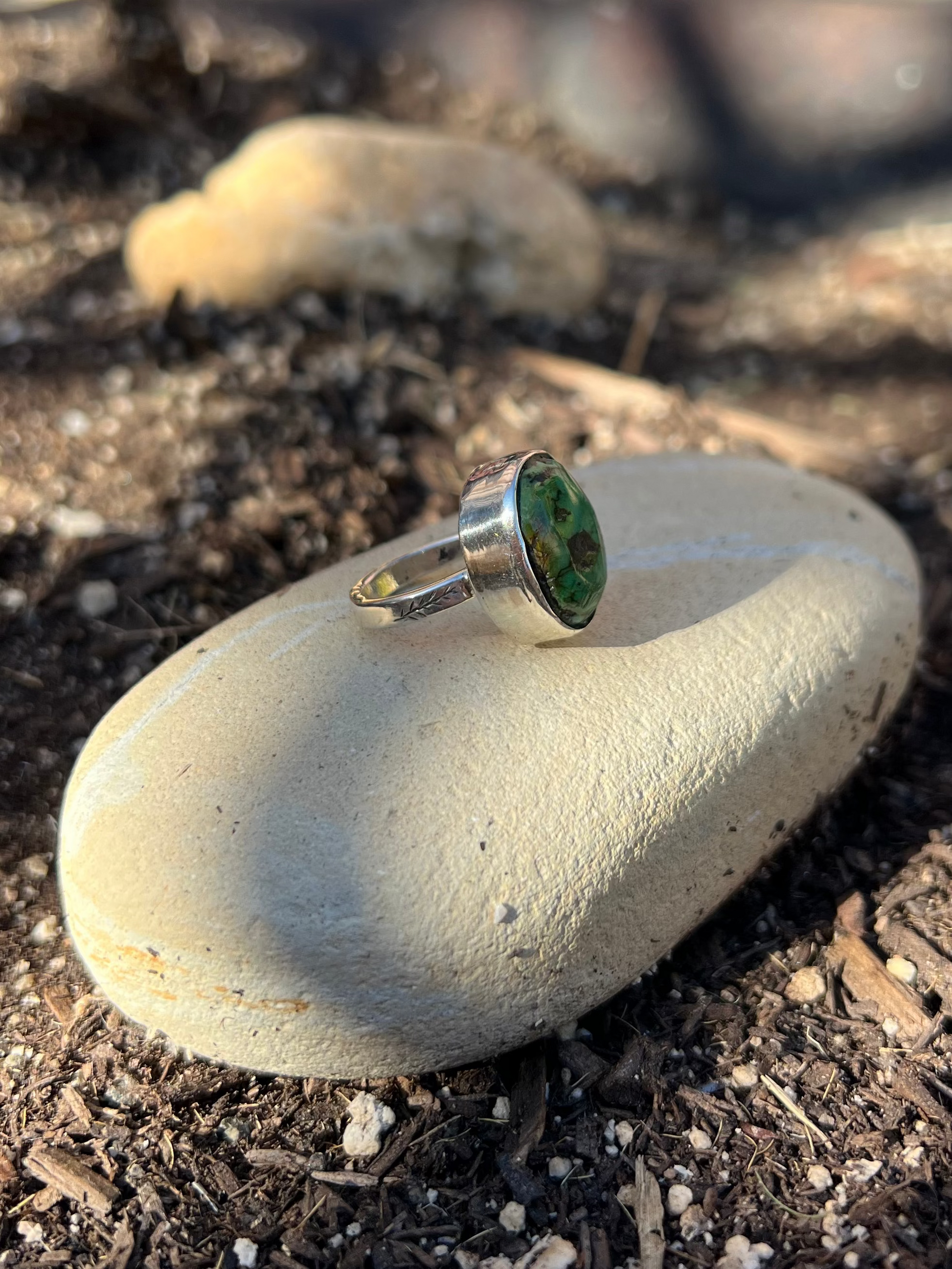 Silver earring with green gemstone on a white stone in a garden setting